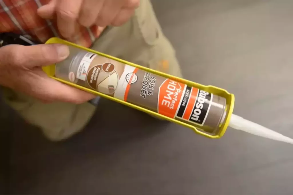 Pose du joint acrylique au pistolet à mastic le long de la plinthe sur parquet